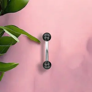 Detail of a curved stainless steel eyebrow ring with black balls against pink texture