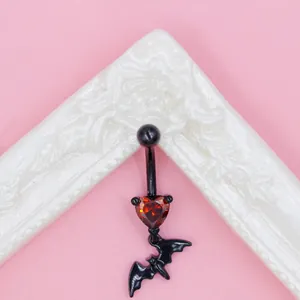 Macro detail of gothic black bat belly ring with sparkling red heart-shaped zircon