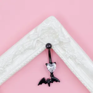 Macro detail of gothic black bat navel ring with a sparkling heart-shaped zircon stone