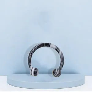 Detailed view of striped acrylic horseshoe ring for nose or ear piercing on blue stage