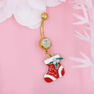Primer plano de un piercing de ombligo dorado con colgante de calcetín navideño rojo