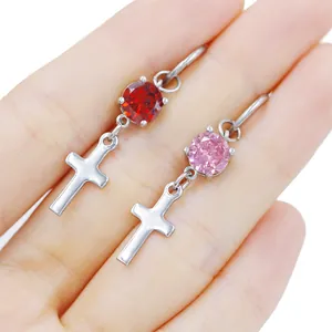 Macro view of stainless steel cross earrings with red and pink gemstones in hand
