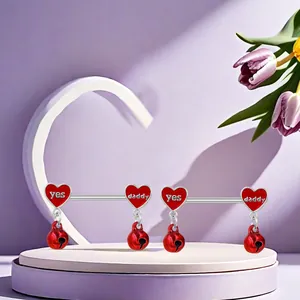 Detail of red heart bells with 'Yes Daddy' engraving on stainless steel nipple rings