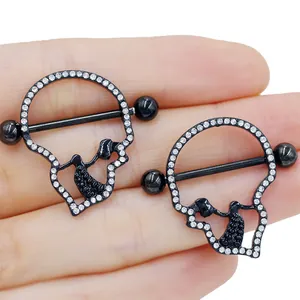 Pair of black skull nipple rings with white crystal accents held by hand