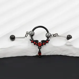 Detailed view of Gothic bat nipple ring with red crystals on white stone background