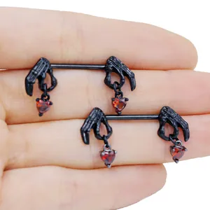 Macro detail of gothic nipple rings featuring black skeletal hands and red heart zircons