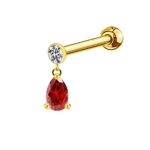 Detail of a golden piercing earring featuring a round zircon and pear-shaped red gemstone