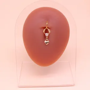 Dettaglio di un piercing all'ombelico dorato con ali di farfalla e cuore