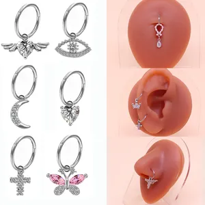 Dettaglio di piercing argentati con ciondoli a cuore, luna e farfalla su modello in silicone