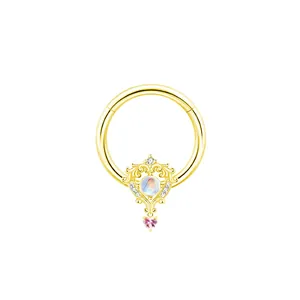 Dettaglio di un anello piercing dorato con pietra di luna e ciondolo a cuore