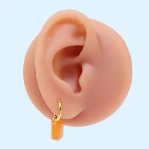 Orecchini a cerchio dorati con pendente rettangolare arancione su modello espositivo