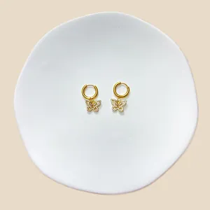 Detailansicht goldener Schmetterlings-Ohrhänger mit Zirkonia auf einer Keramikschale