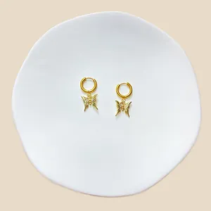 Nahaufnahme von goldenen Schmetterling-Ohrringen mit weißen Kristallen auf weißem Display