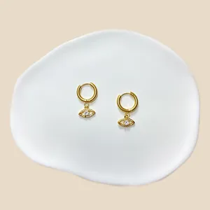 Nahaufnahme goldener Creolen mit Kristall-Augen-Anhängern auf einem Keramiktablett