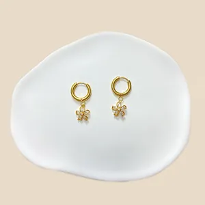 Detailaufnahme goldener Creolen mit Zirkonia-Blumenanhängern auf einer Keramikschale