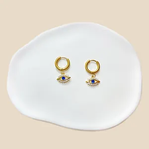 Detailansicht der goldenen Evil Eye Ohrringe mit blauen Steinen auf weißer Keramikschale
