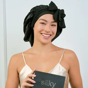 Detail of black silk sleep bonnet with bow accent and packaging held by a model