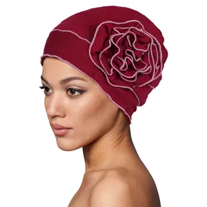 Detail of burgundy turban cap featuring a large 3D floral accent with pink stitched edges