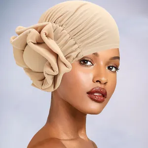 Detail of elegant pleated turban hat featuring a large 3D fabric flower in beige