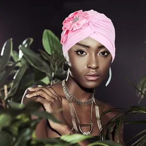 Pink pleated turban cap with satin flower and rhinestone brooch shown on a model