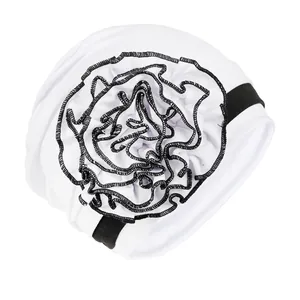 Detail of white turban hat featuring a 3D layered flower with black embroidered edges