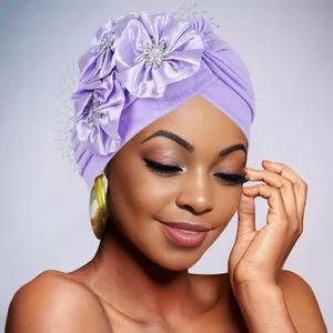 Detail of purple turban cap featuring 3D satin flowers, rhinestones, and black mesh veil