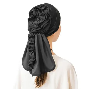 Detail of elegant black turban featuring a large 3D layered flower and wavy long tail