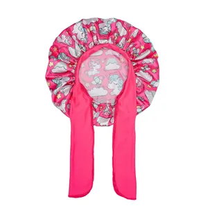 Detail of pink satin sleep cap featuring unicorn patterns and long ribbon ties for hair care