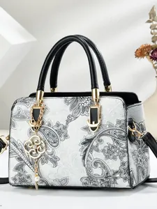White tote bag with black paisley patterns, gold hardware, and pearl pendant detail