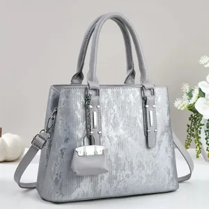 Detail of silver metallic tote bag with textured finish, dual handles and mini charm