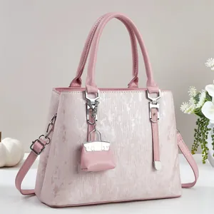 Close-up of pink handbag with metallic grain finish, silver hardware, and mini bag charm