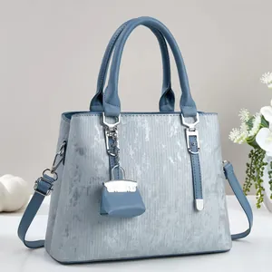 Detailed view of grey blue leather handbag with silver chain and mini charm bag accessory