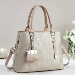 Detail of cream luxury handbag showing metallic texture and creative mini bag charm