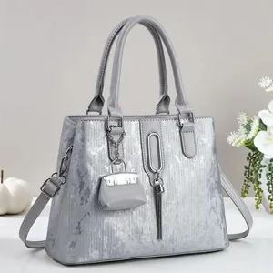Detailopname van zilveren tote tas met metalen kwastje en mini tasvormige accessoire