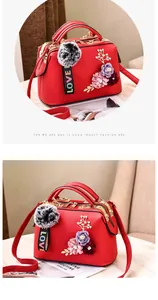 Makro-Detail einer roten Ledertasche mit Blumenstickerei und weichem Pelzball-Anhänger