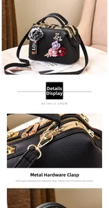 Details von Blumenstickerei, goldenem Metallverschluss und Plüschball an schwarzer Tasche