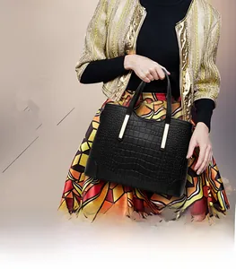 Detail of black crocodile pattern leather tote bag with gold metal trim and top handles