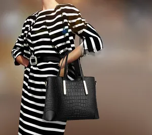 Detail of black faux crocodile texture handbag with gold hardware held by model