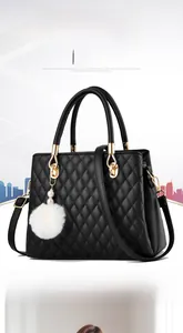 Detail of diamond quilted stitching and fur pom-pom charm on black leather handbag