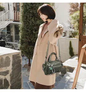 Detail of dark green Boston bag with star charm and leather texture on beige coat