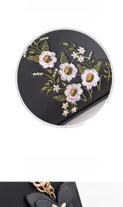 Close-up of floral embroidery and gold butterfly pendant on black leather handbag