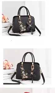 Close-up of floral embroidery on a black faux leather handbag with a butterfly charm