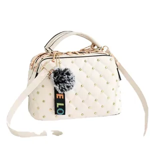 White quilted crossbody bag with gold rivets and black pompom charm on white background