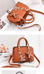 Detail of brown PU leather handbag featuring floral embroidery and butterfly pendant charm