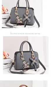 Detailed close-up of dark grey crossbody bag with floral embroidery and bow charm