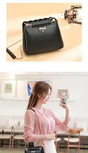 Detail of black crossbody bag with wave edge, metal bow, and chain strap shown on model