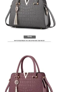 Detail of grey crocodile embossed handbag featuring a metal V logo and tassel pendant
