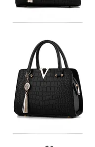 Detail view of black crocodile pattern handbag with gold V logo and metal tassel