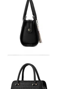 Close-up of black handbag detailing crocodile texture, tassel charm and golden hardware