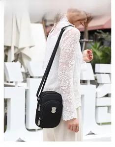 Dettaglio borsa a tracolla nera in nylon per cellulare con logo in metallo e tasche a zip